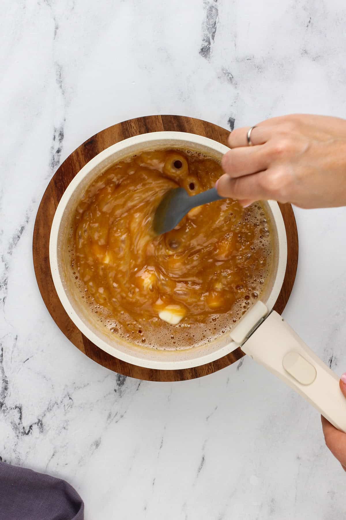 Hand stirring butter and cream cheese into caramel sauce.