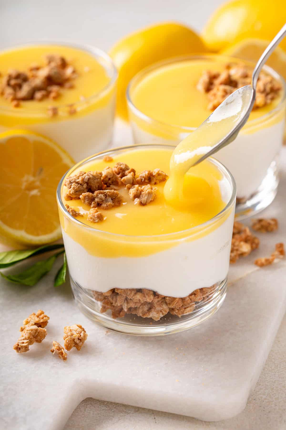 Lemon curd being spooned on top of a ramekin of cheesecake.