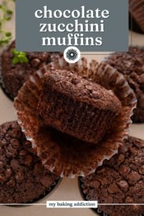 Unwrapped chocolate zucchini muffins perched on cooled muffins in a muffin tin. Text overlay includes recipe name.