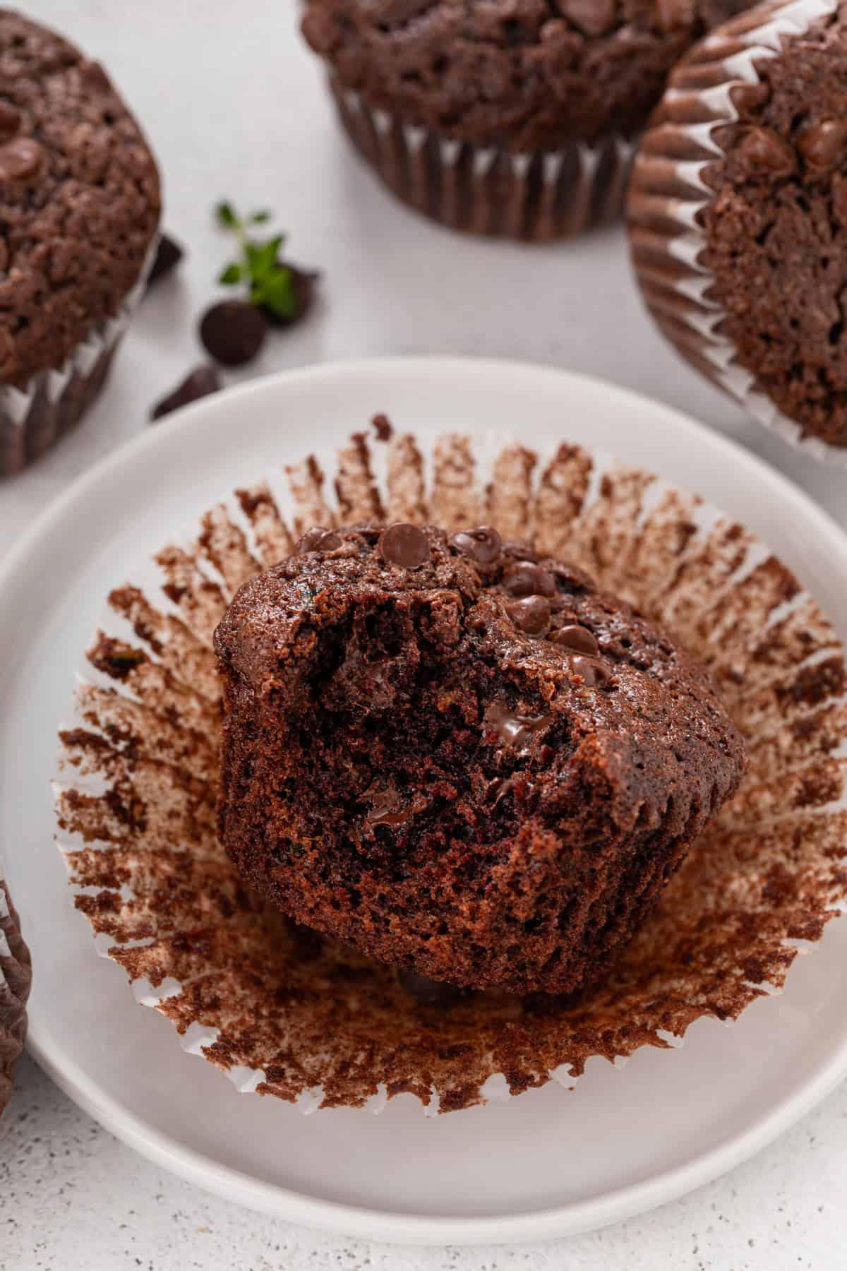 Bite taken from an unwrapped zucchini muffin on a white plate.