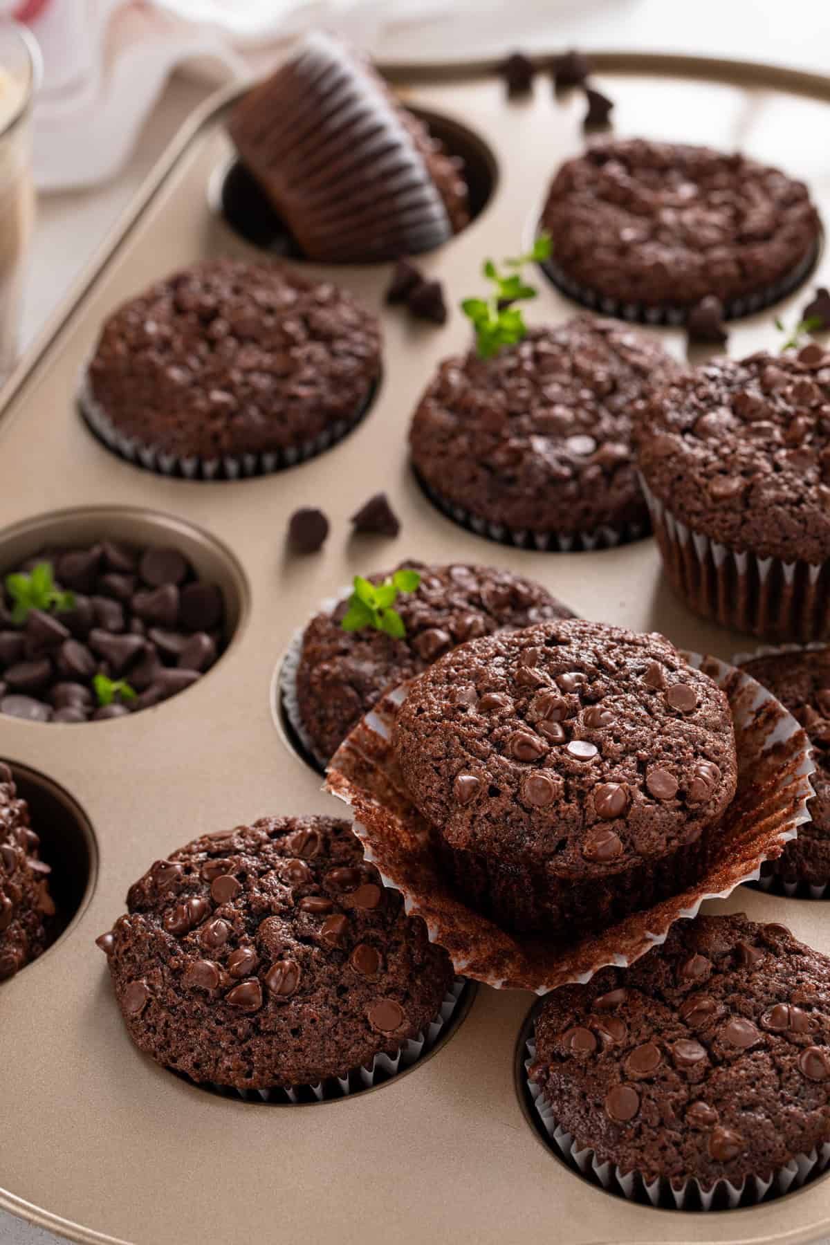 Chocolate zucchini muffins arranged in and on top of a muffin tin.