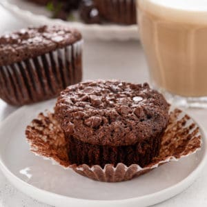 Unwrapped chocolate zucchini muffin on a white plate.