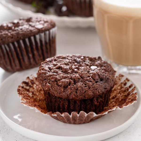 Unwrapped chocolate zucchini muffin on a white plate.
