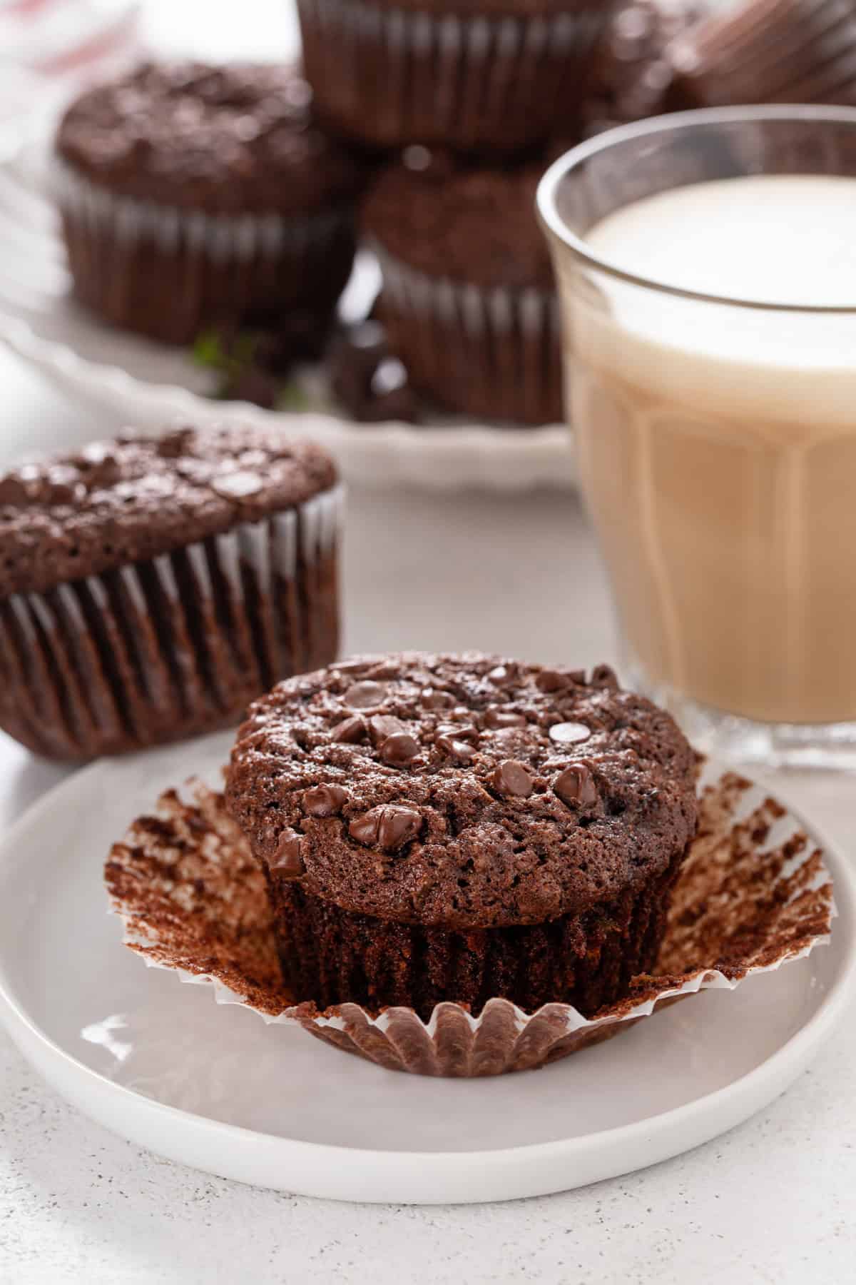 Plated chocolate zucchini muffin with a cup of coffee in the background.