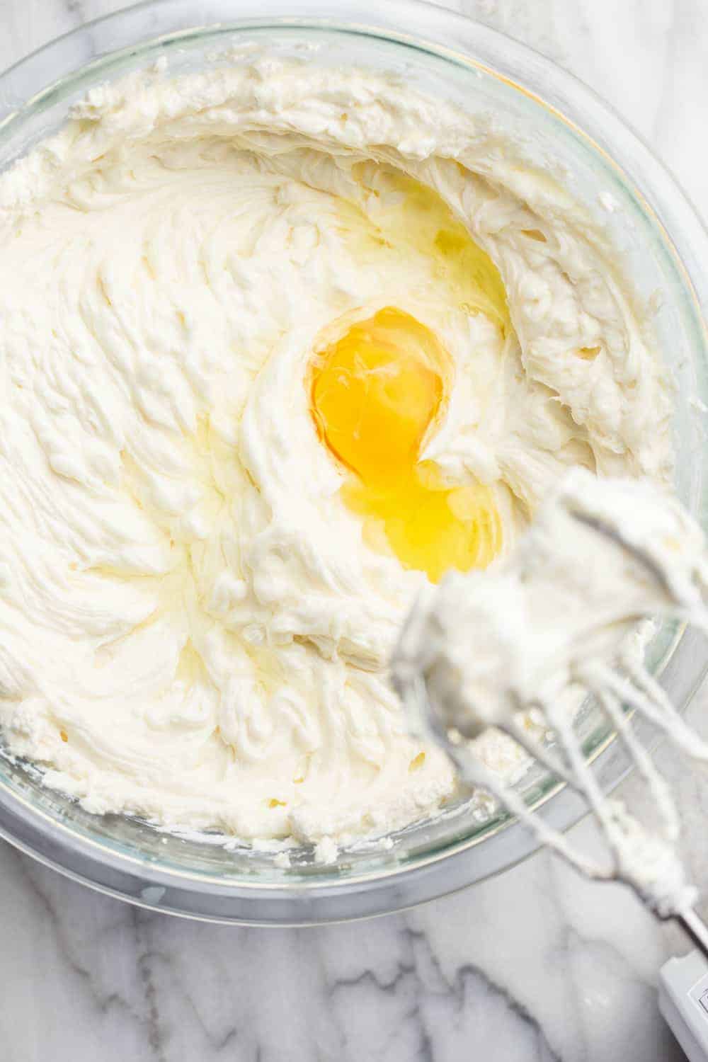 Adding eggs to vanilla cheesecake filling and mixing with an electric mixer