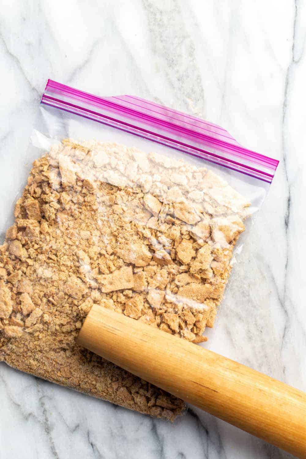 Rolling pin crushing graham crackers in a zip-top bag into crumbs