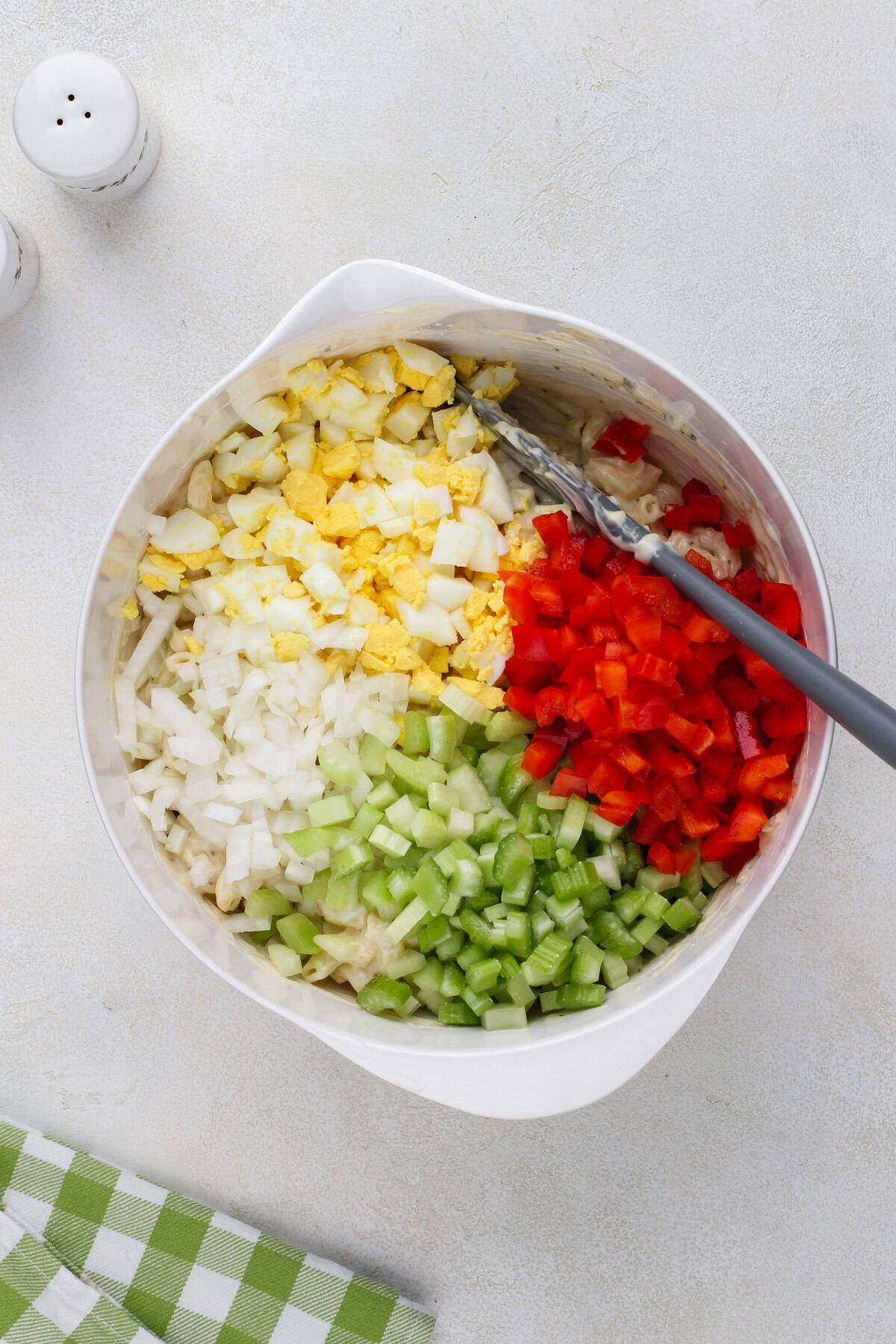 Eggs, celery, onions, and pepper added to a bowl of macaroni salad.