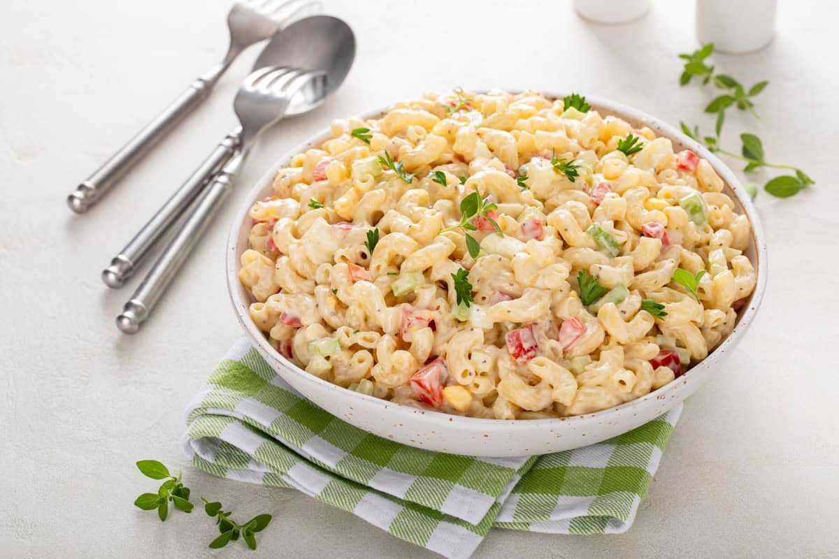 White serving bowl holding macaroni salad, set on a green and white napkin.
