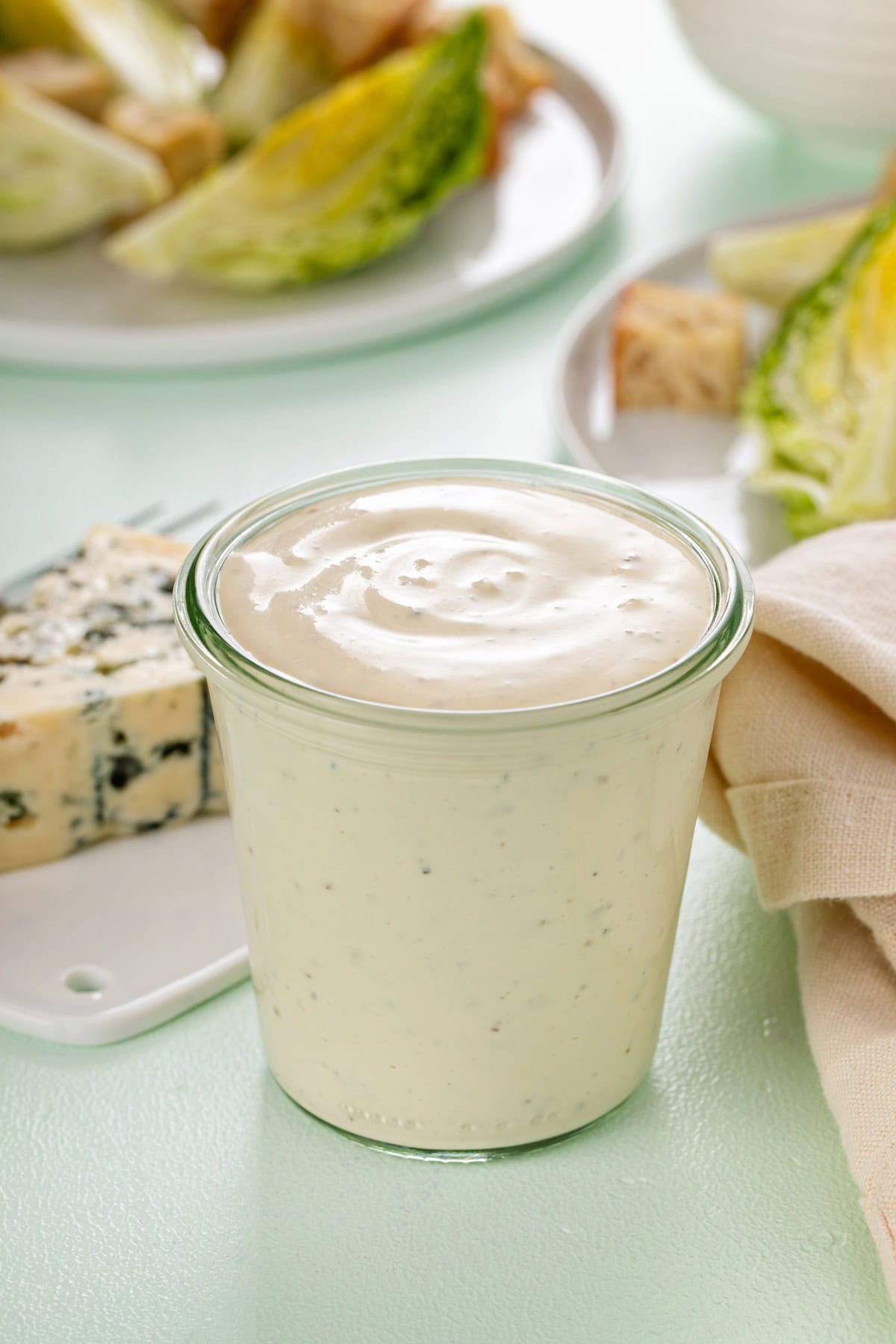 Glass jar filled with blue cheese dressing, with a chunk of blue cheese in the background.