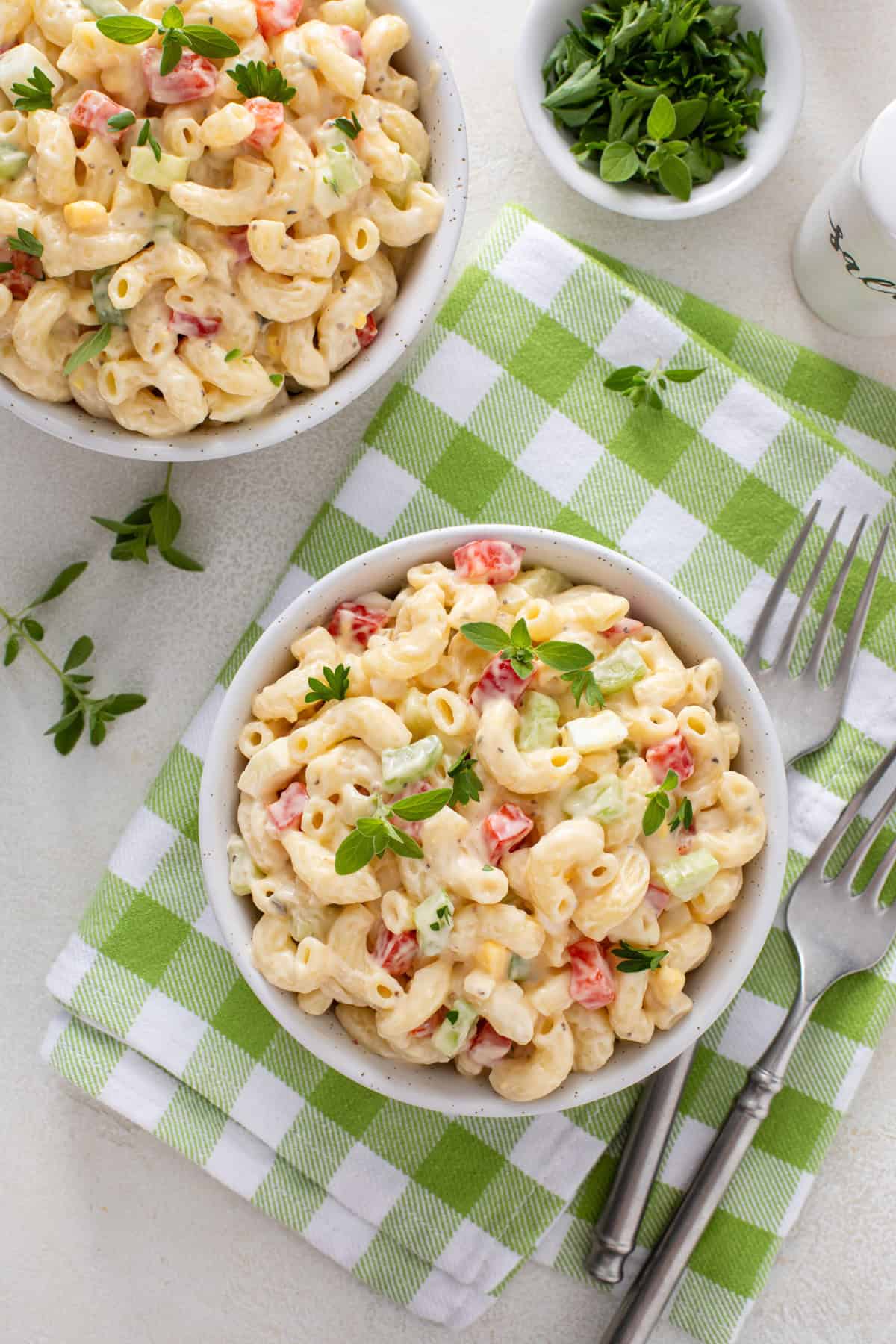 Overhead view of two small bowls of amish macaroni salad on a green and white napkin.