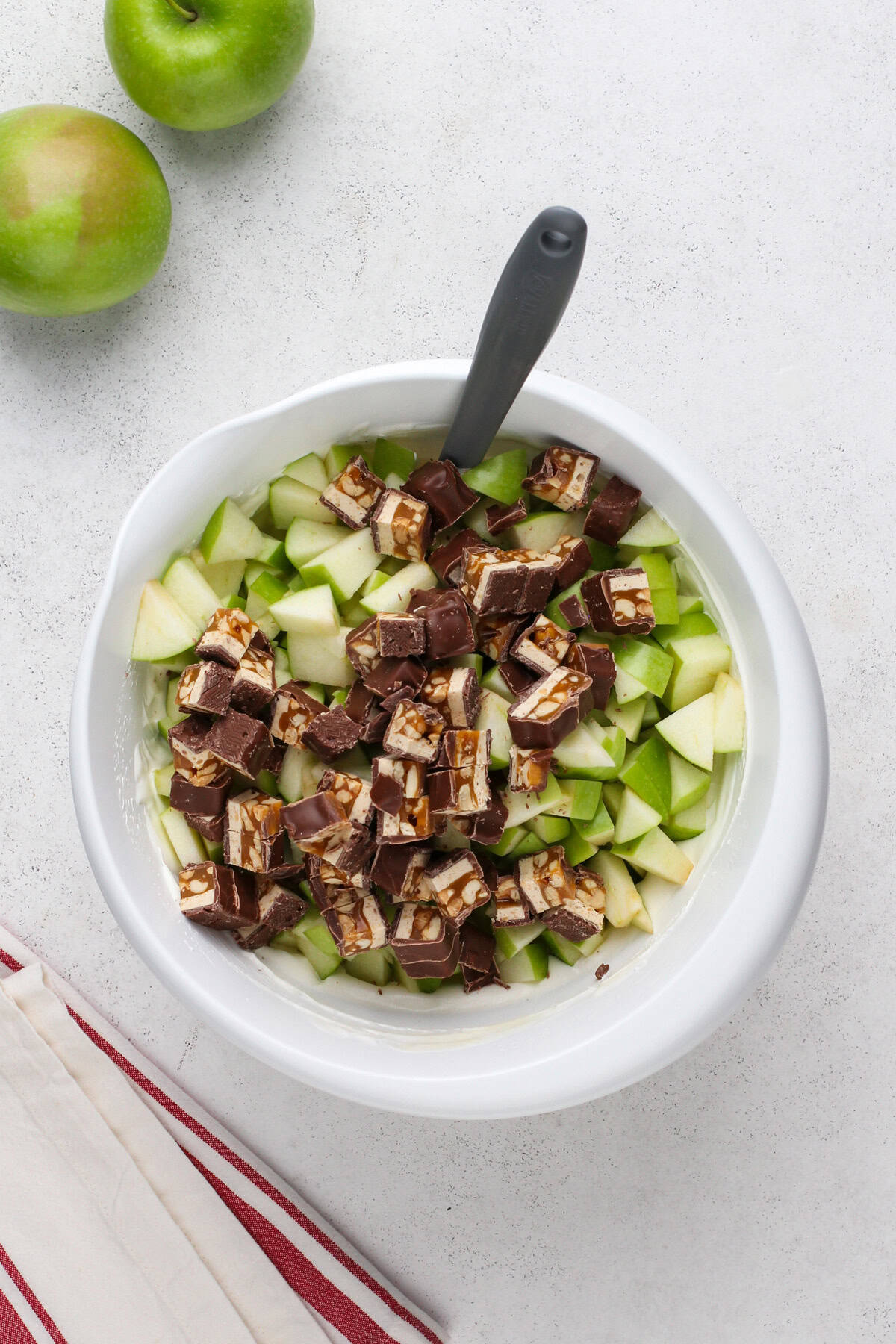 Chopped green apples and snickers bars added to a white mixing bowl.