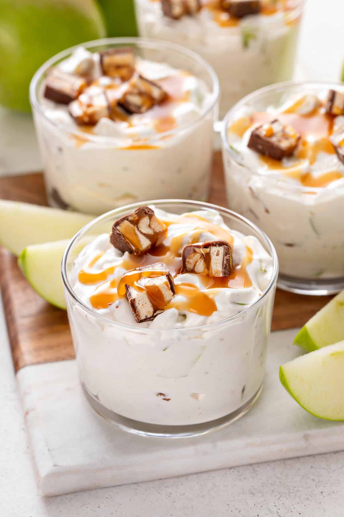 Several small glass bowls filled with snickers apple salad, each garnished with pieces of snickers and salted caramel sauce.
