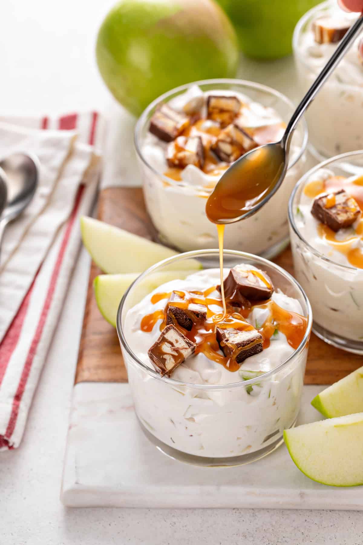 Spoon drizzling salted caramel sauce over a small bowl of snickers apple salad.