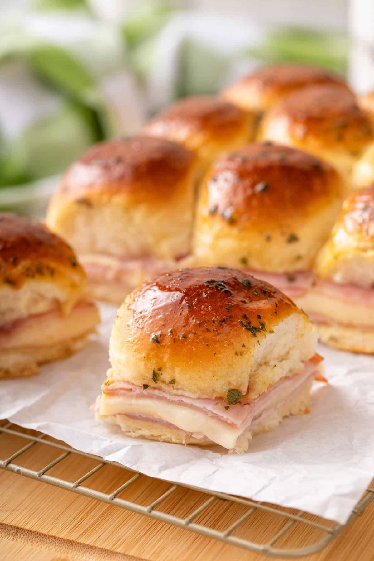 Close up of a ham and cheese slider set on a piece of parchment paper with more sliders in the background.