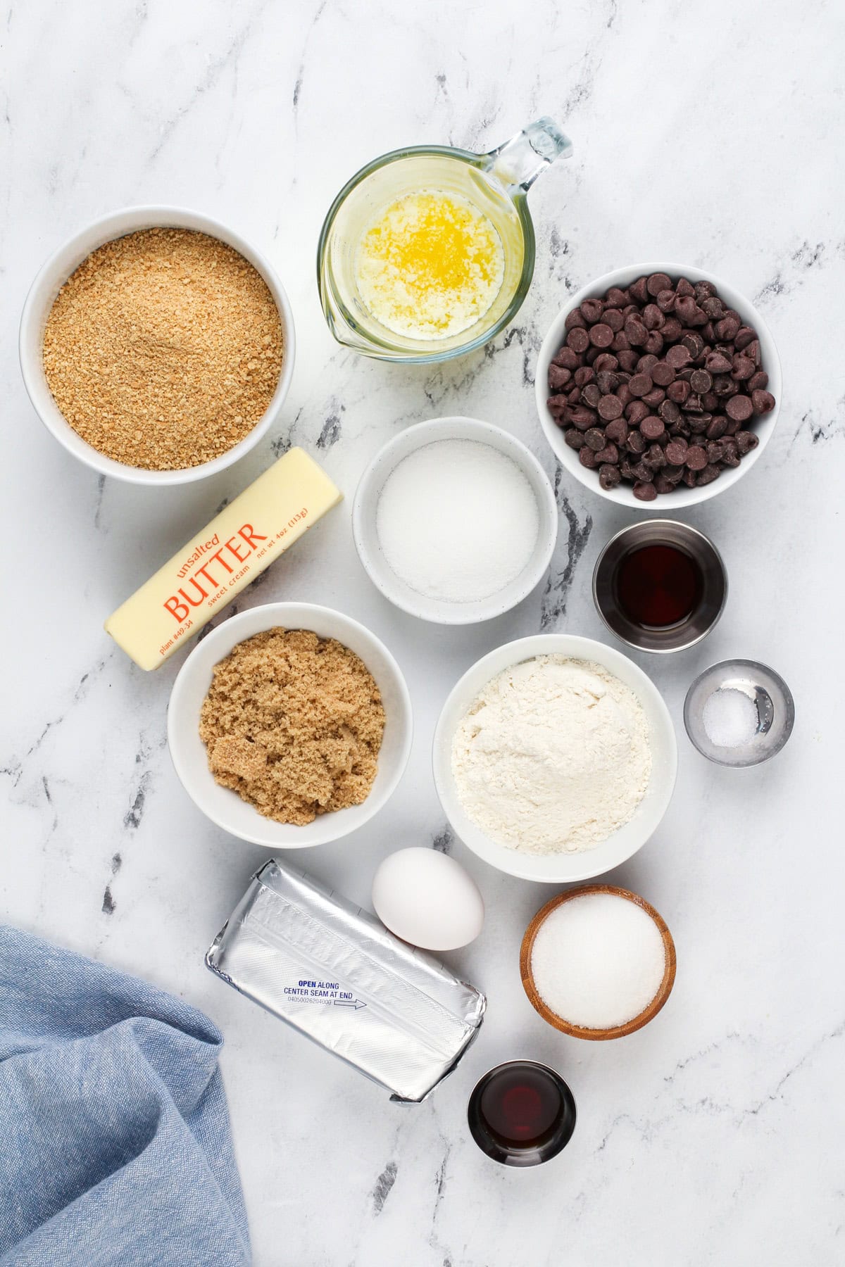 Ingredients for cookie dough cheesecake bars arranged on a marble counter.
