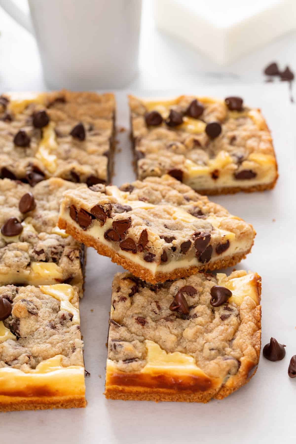 Close up of a cookie dough cheesecake bar leaning on other sliced bars on a white board.