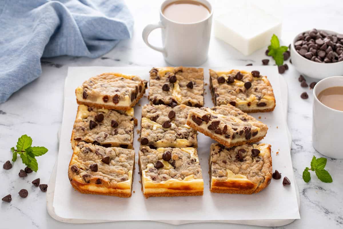 Sliced batch of cookie dough cheesecake bars on a white board in front of a cup of coffee.