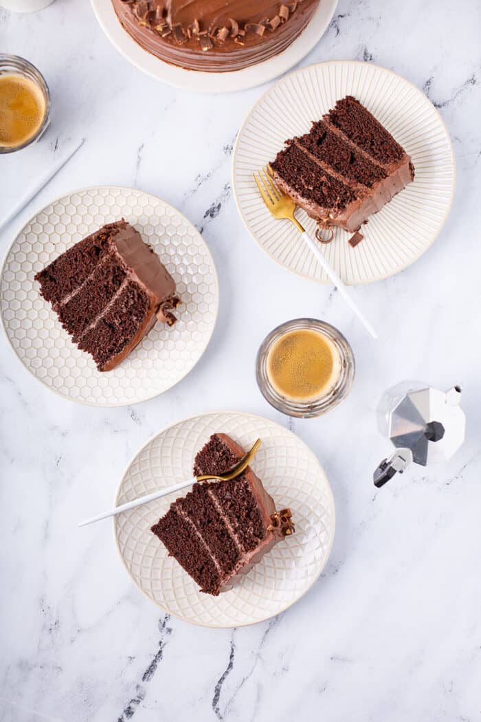Overhead view of 3 slices of Hershey's chocolate cake on white plates with cups of espresso