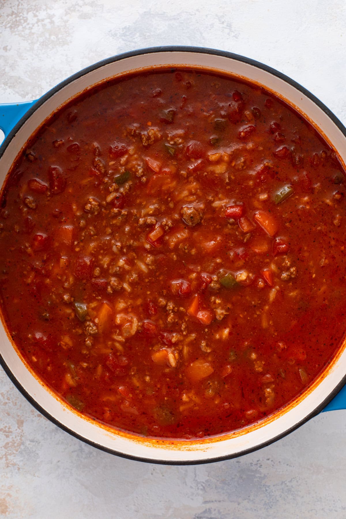 Rice added to stuffed pepper soup in a blue dutch oven.