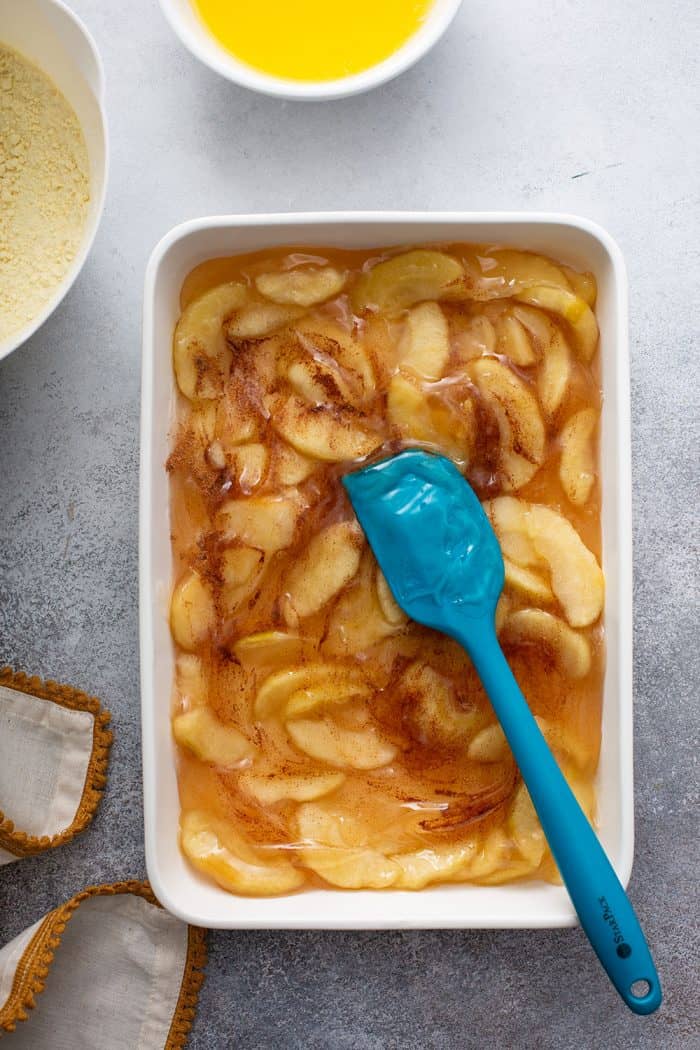 Spatula spreading apple pie filling into a white cake pan