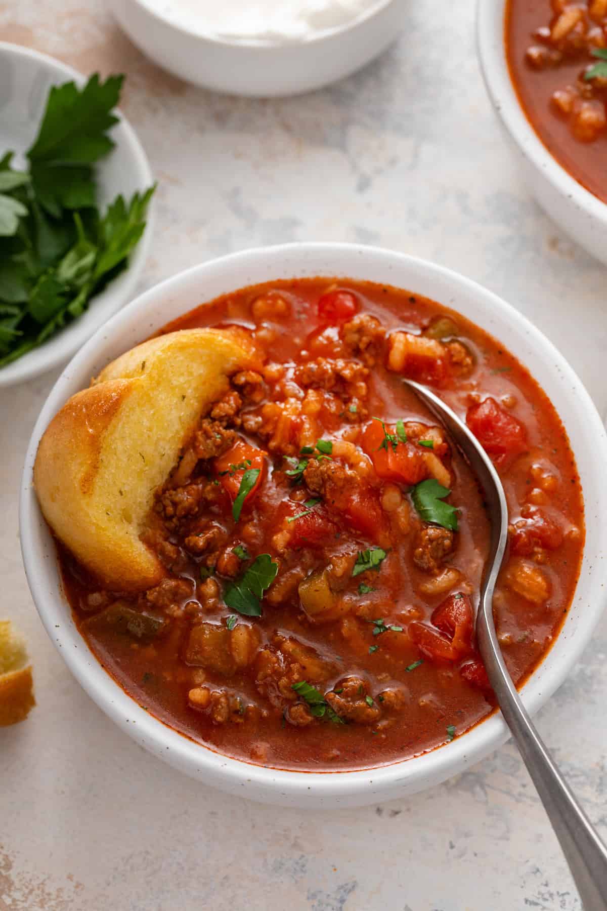 A slice of texas toast and a spoon in a white bowl of stuffed pepper soup.
