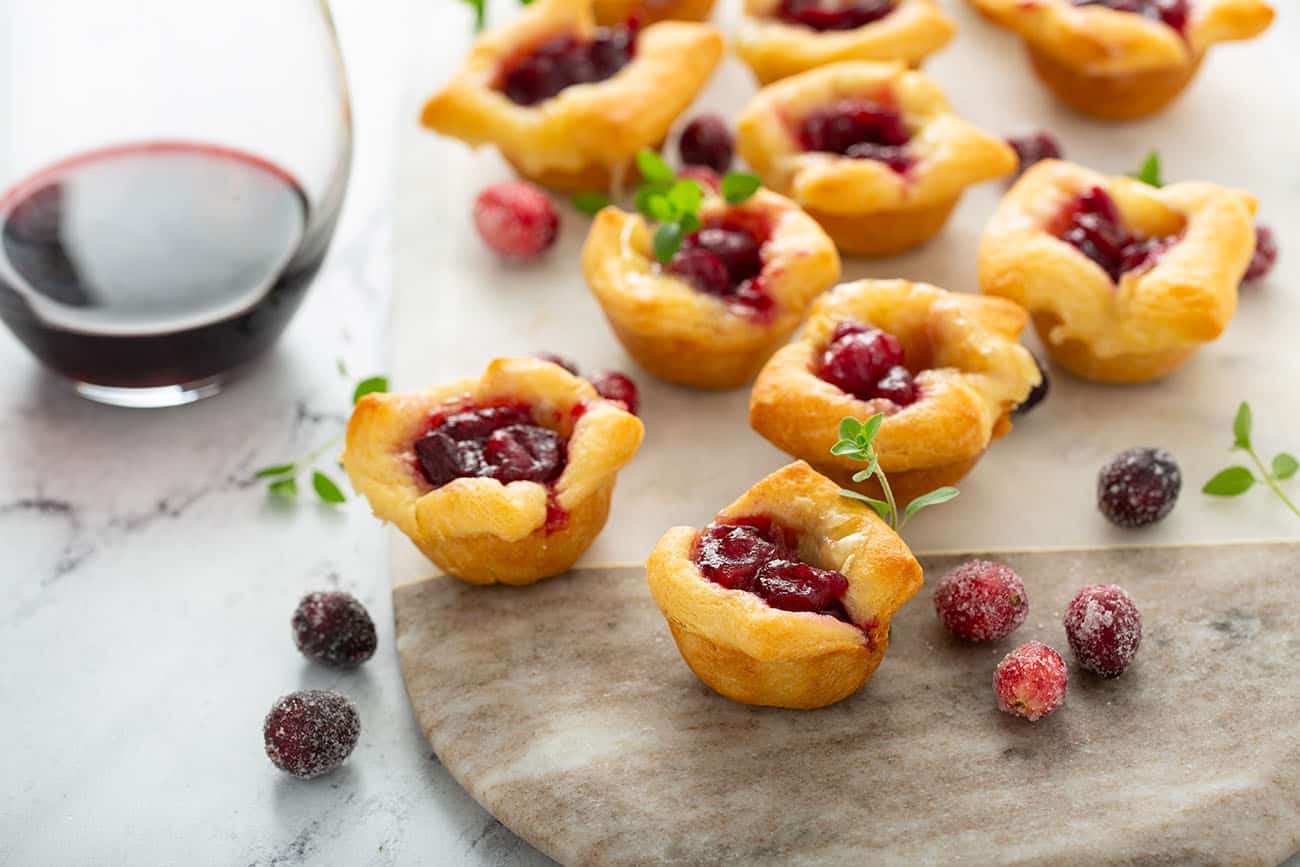 Cranberry Brie Bites arranged on a wood and marble board next to a glass of red wine