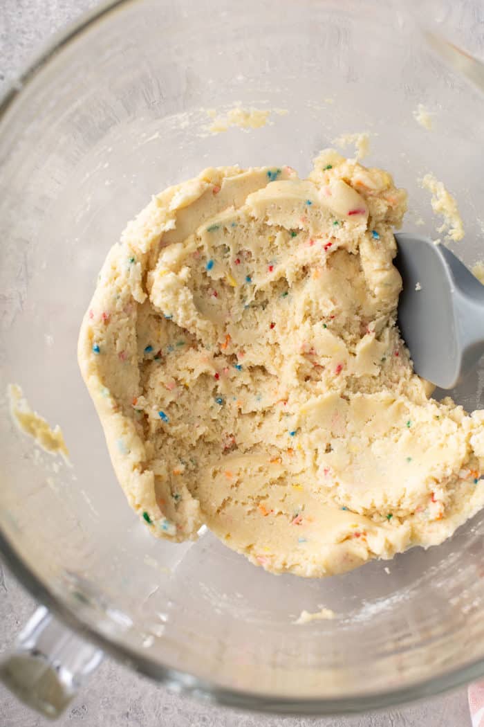 Spatula stirring funfetti cookie dough in a glass mixing bowl