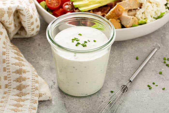 Jar of homemade ranch dressing next to a bowl of salad