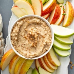 Overhead view of a bowl of toffee apple dip surrounded by fresh apples on a white platter