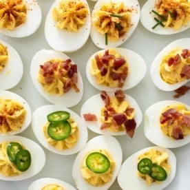 Close up of deviled eggs on a platter, topped with a variety of garnishes