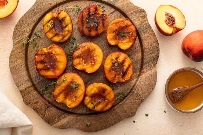 Grilled peach halves set on a wooden platter.