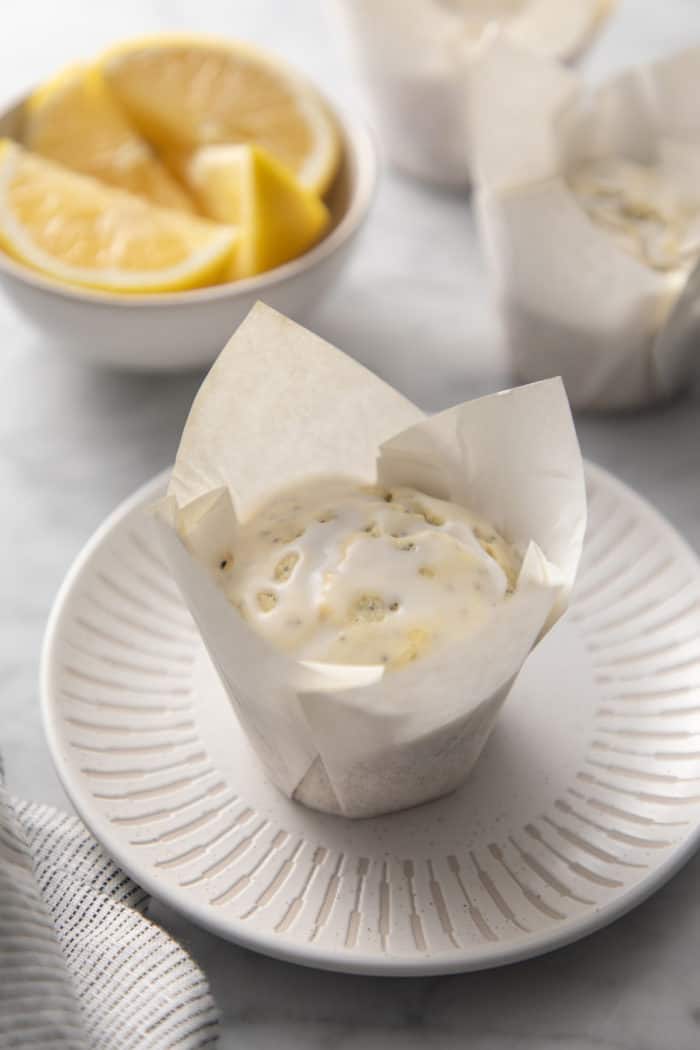 Glazed lemon poppy seed muffin in a parchment wrapper set on a white plate.