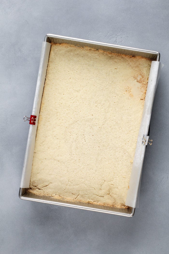 Baked shortbread crust for coconut cream bars in a lined metal baking pan.