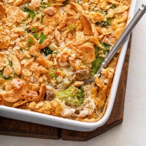 Serving spoon in the corner of a baking dish full of chicken broccoli rice casserole.