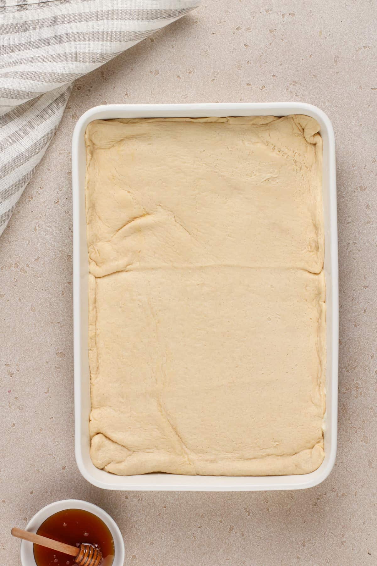 Crescent roll dough on top of cheesecake filling in a white pan.