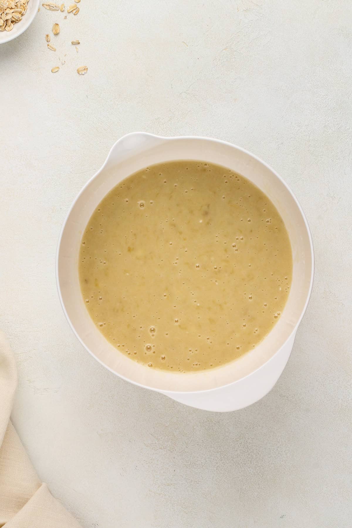 Wet ingredients for oatmeal banana bread mixed in a white bowl.