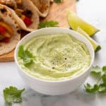 Avocado crema in a white bowl, garnished with cilantro.