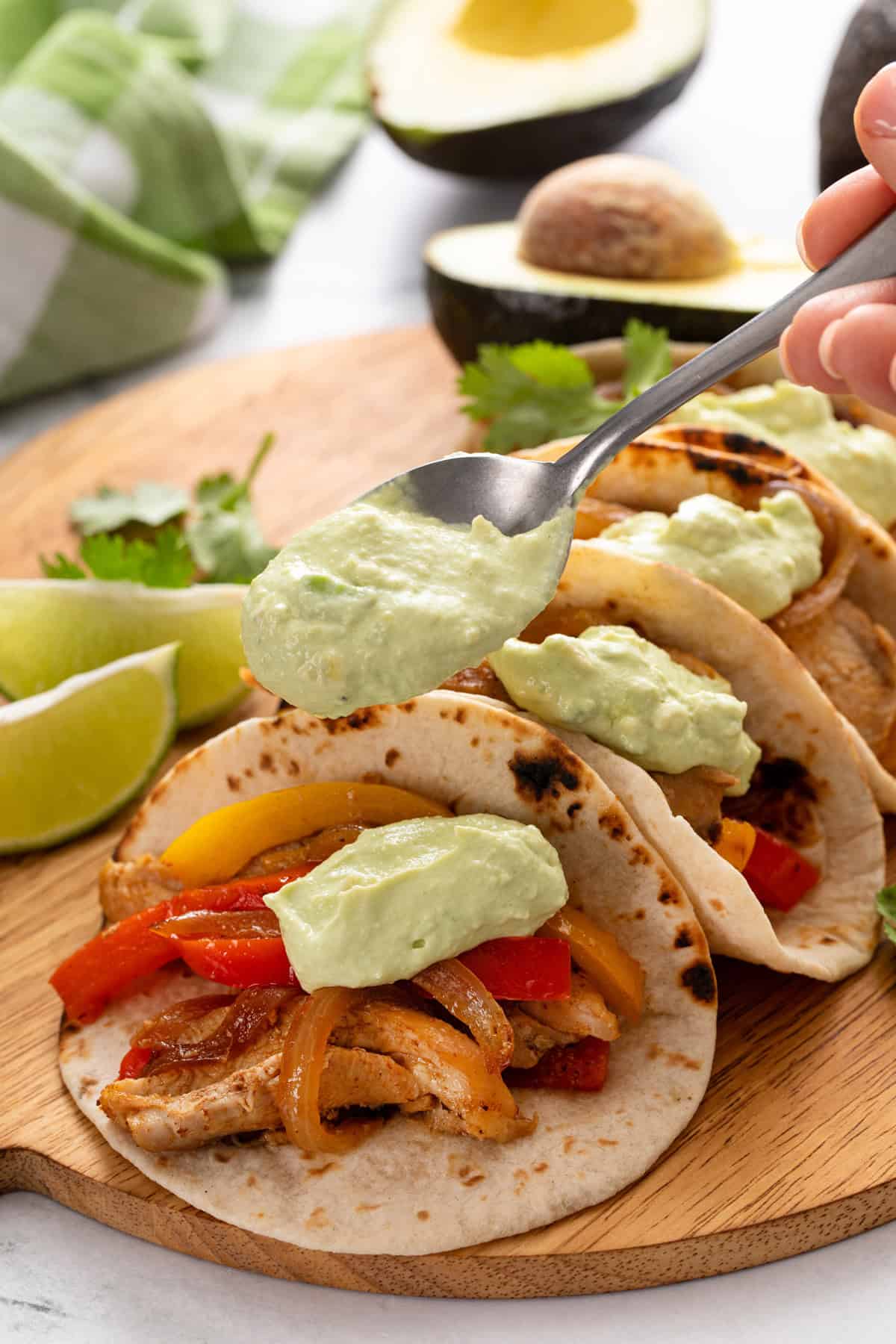 Spoon topping chicken tacos with avocado crema.