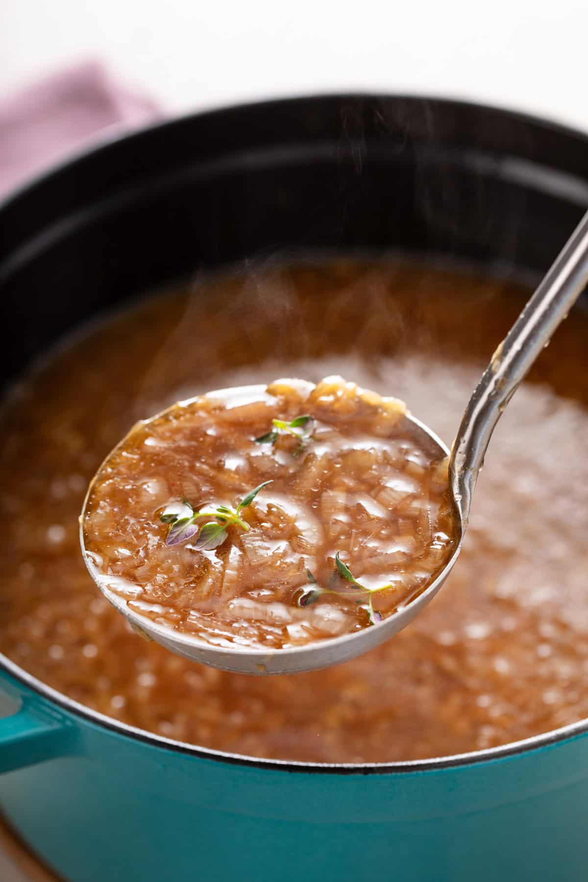 Ladle holding up french onion soup over a pot of the soup.