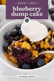 Close up of a spoon in a bowl of blueberry dump cake topped with a dollop of whipped cream. Text overlay includes recipe name.