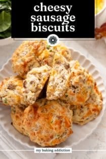 Cheesy sausage biscuits arranged on a white platter, with the biscuit on top broken in half. Text overlay includes recipe name.