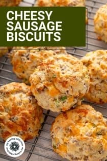 Close up of cheesy sausage biscuits stacked on a cooling rack. Text overlay includes recipe name.