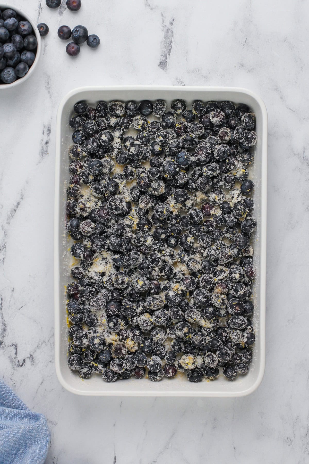 Blueberries tossed with sugar and lemon zest in a baking pan.