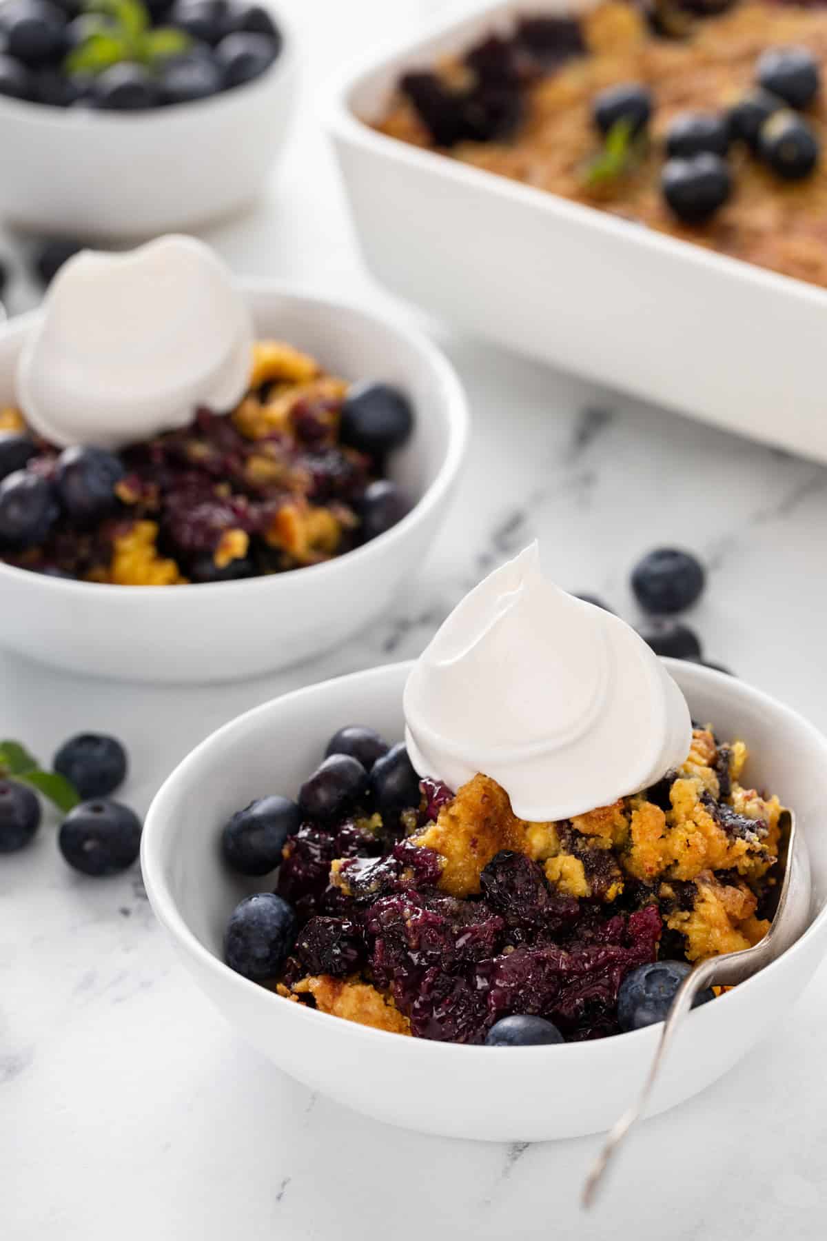 Two white bowls filled with blueberry dump cake topped with whipped cream.