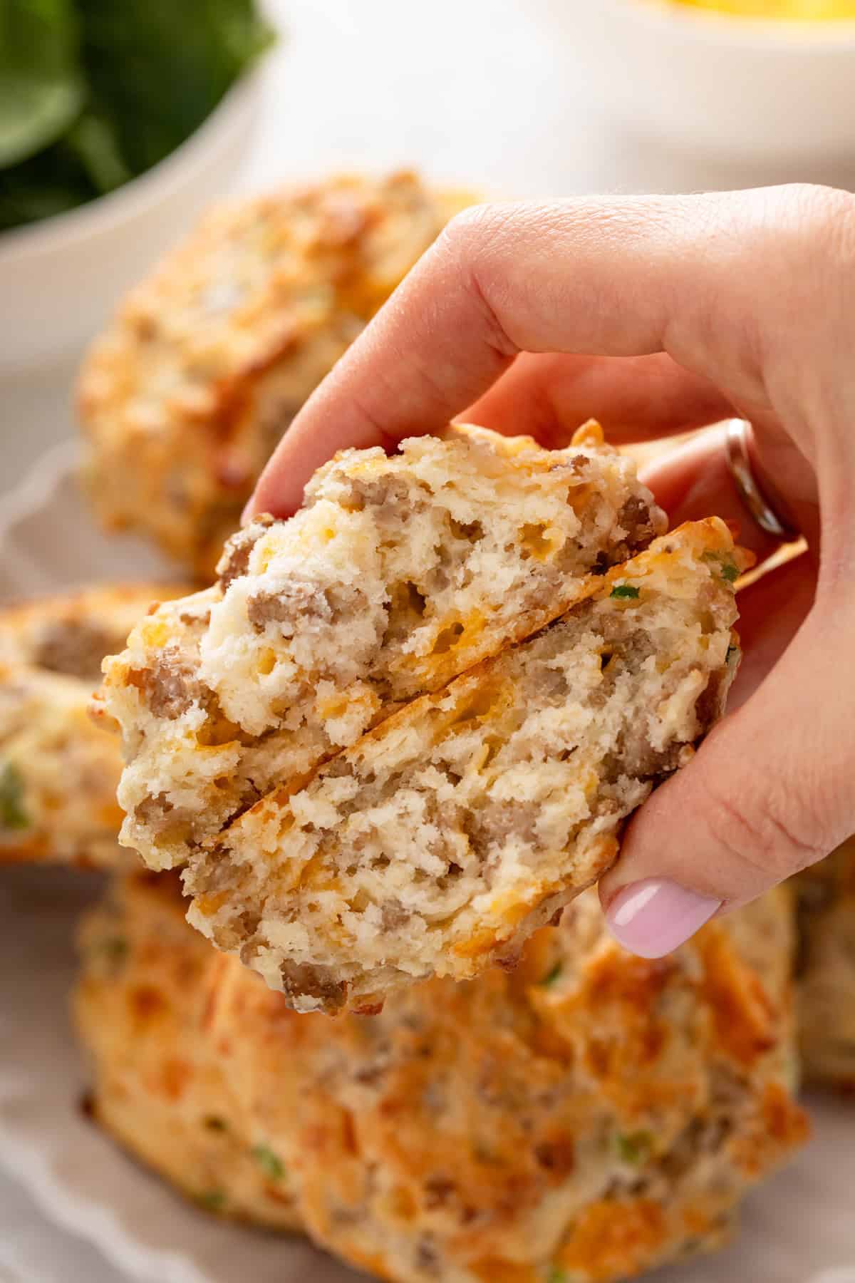 Hand holding up a halved cheesy sausage biscuit to show the inside texture.