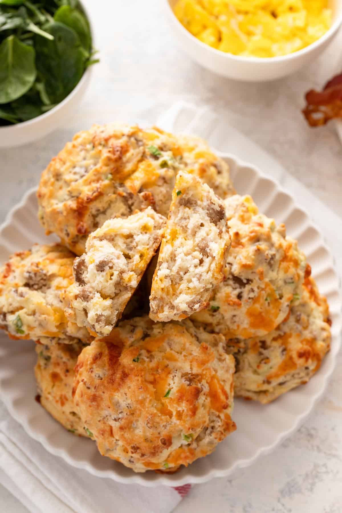 Cheesy sausage biscuits arranged on a white platter, with the biscuit on top broken in half.