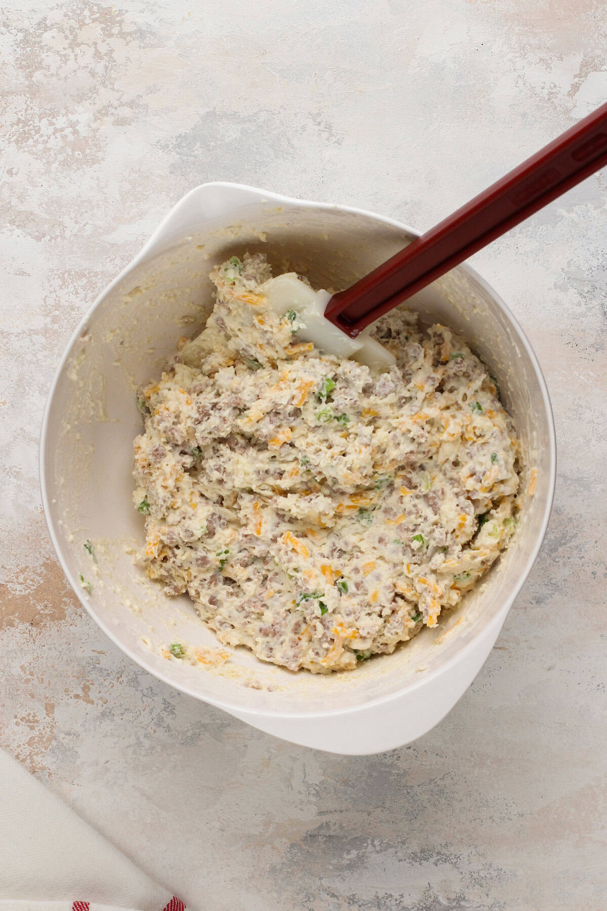 Dough for cheesy sausage biscuits mixed in a white bowl.