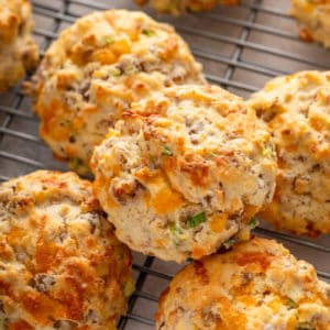 Cheesy sausage biscuits stacked on a wire rack.