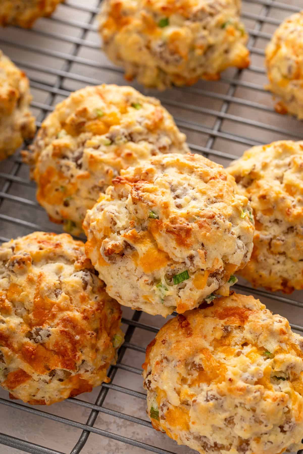 Close up of cheesy sausage biscuits stacked on a cooling rack.