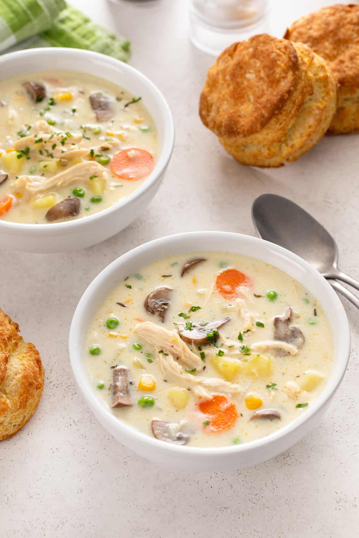 Chicken pot pie soup in two bowls with biscuits next to them.